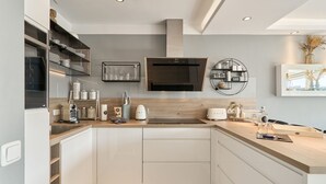 A modern kitchen with white cabinets, a built-in oven, a microwave, and a coffee maker. There is a wooden countertop and a sink.