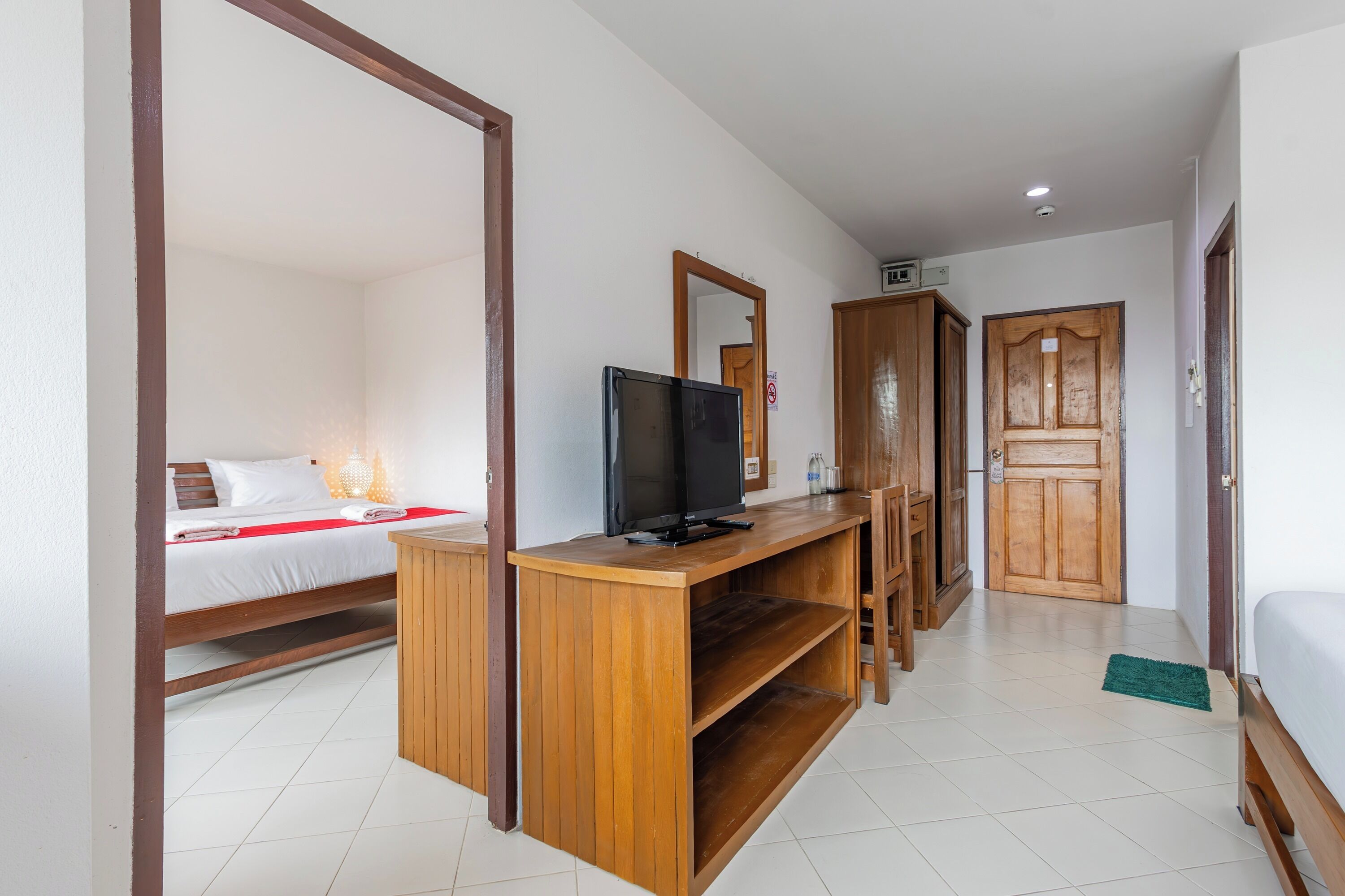 A hotel room with a wooden desk, a television, a bed with white bedding, and a wooden wardrobe.