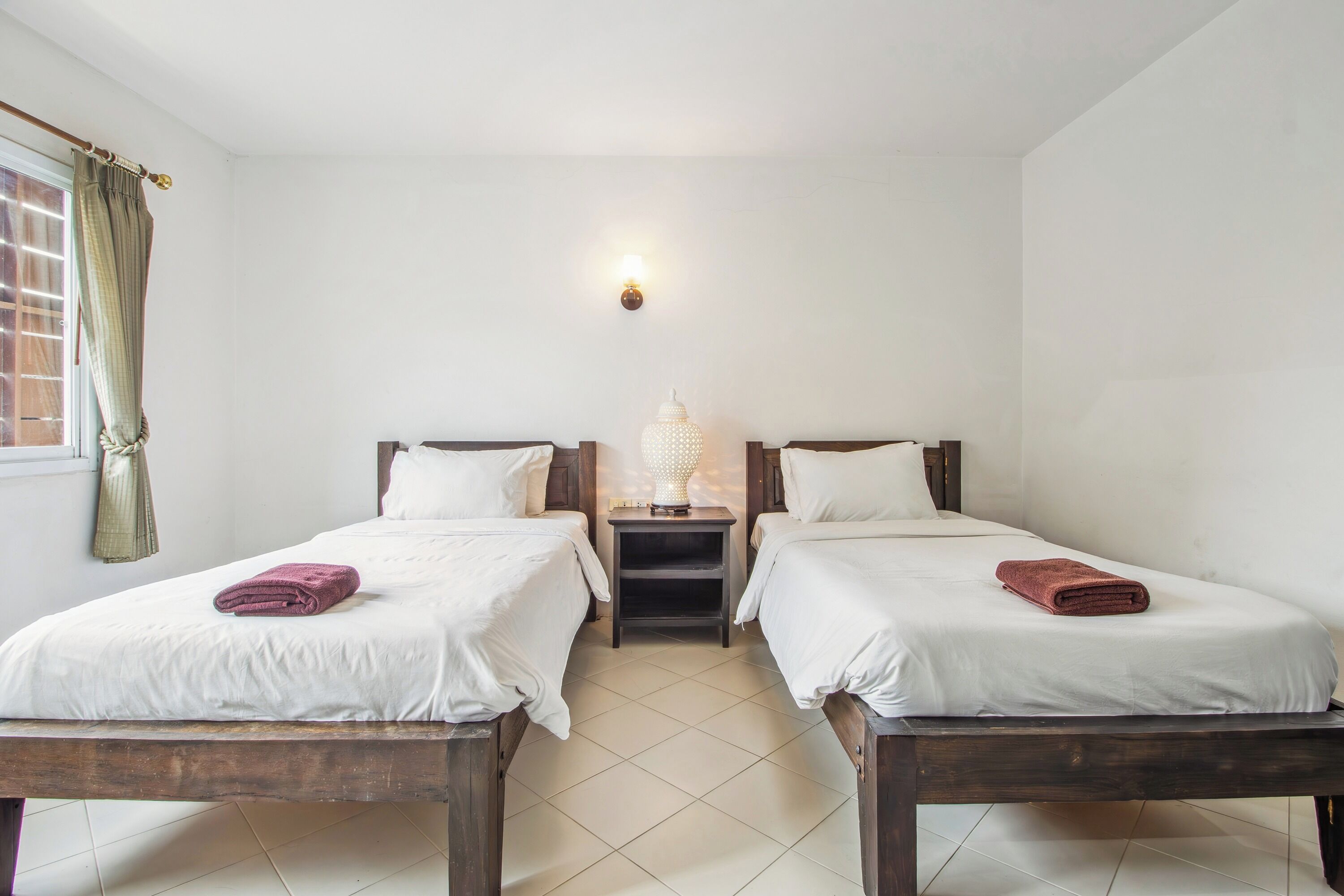 A hotel room with two single beds, a nightstand with a lamp, and a window with curtains.