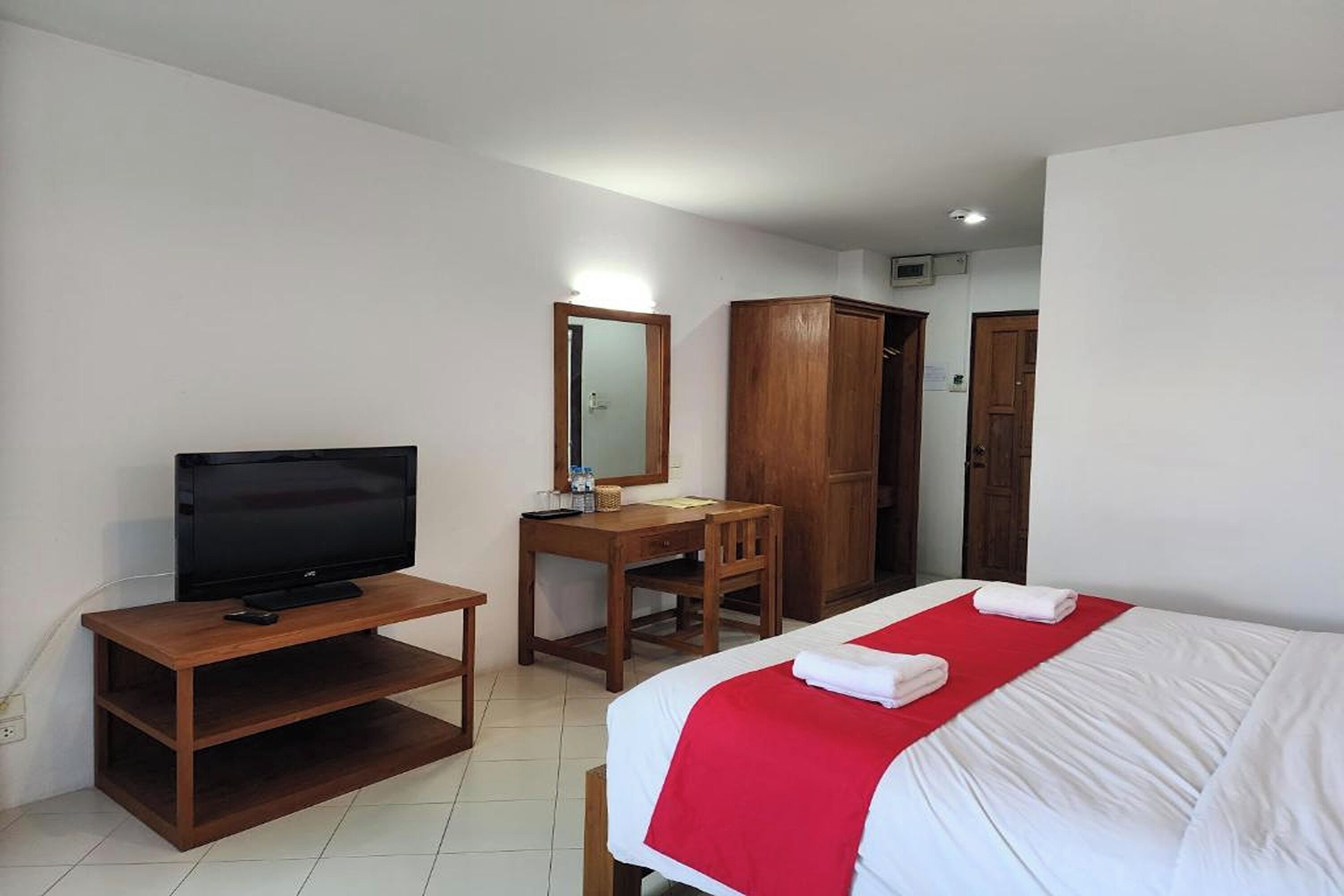 A hotel room with a bed, a TV on a wooden stand, a desk with a chair, and a wardrobe.