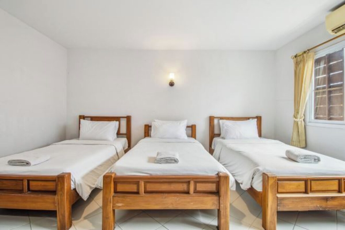 Una habitación con tres camas de madera alineadas contra una pared blanca, cada una con ropa blanca y una toalla doblada.