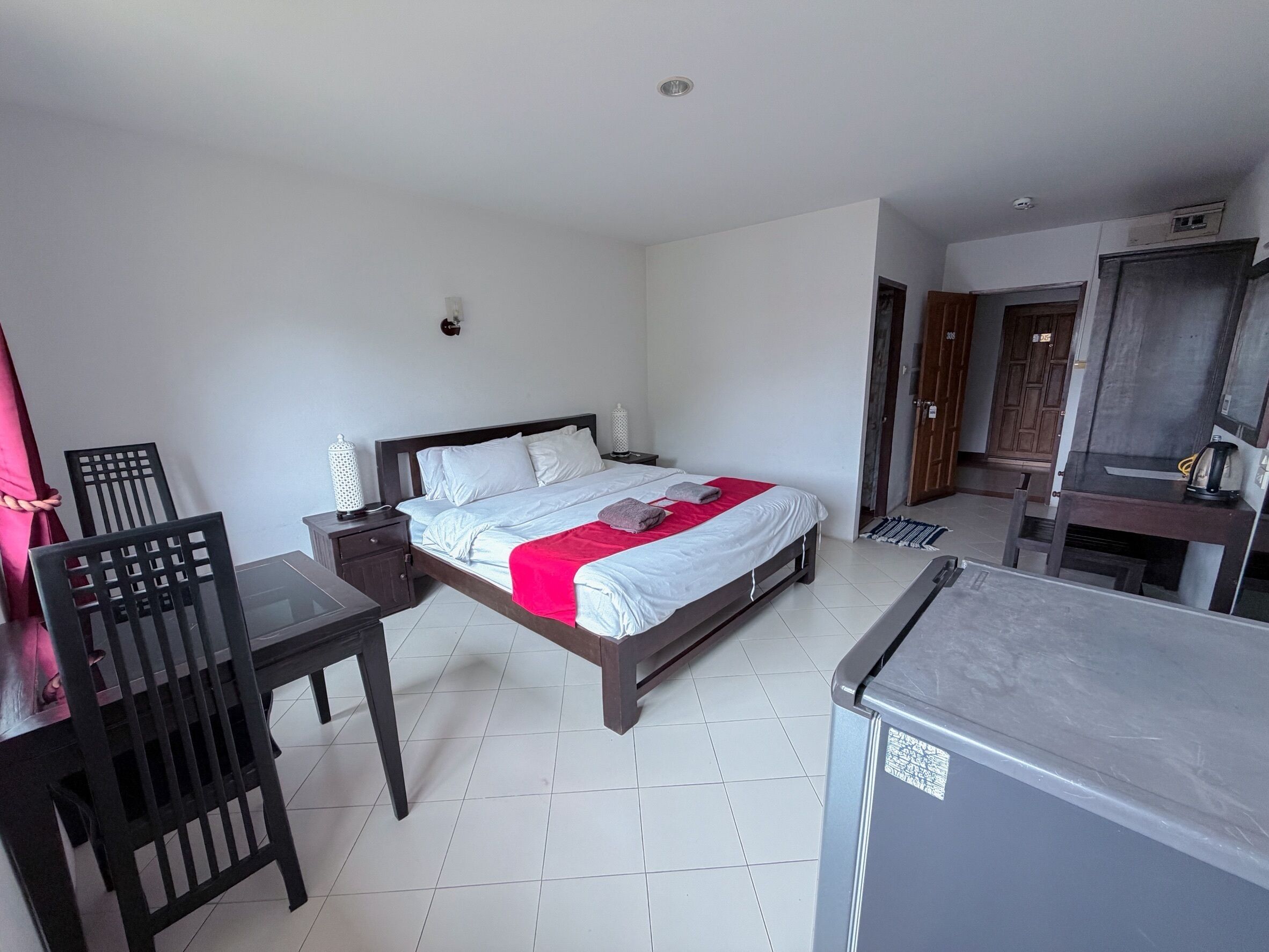 Un dormitorio con cama, escritorio, silla, televisor y kitchenette.