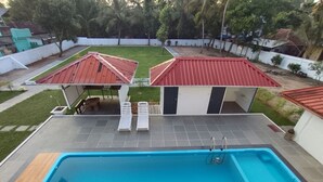 A swimming pool with a tiled deck, two sun loungers, and a covered seating area with a red roof. - The Reds Heritage.
Spacious rooms, vast gardens with a refreshing pool. (Kochi)