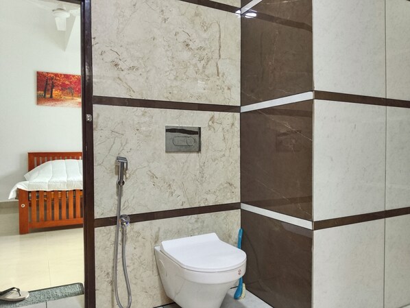 A bathroom with a toilet, shower, and a wooden bed in the adjacent room.