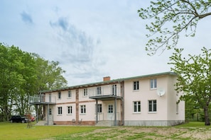 Een gebouw met twee verdiepingen, een balkon op de bovenste verdieping, een bakstenen gedeelte beneden en een schotelantenne aan de rechterkant.