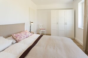 Un dormitorio con cama, una silla, un escritorio y un armario.