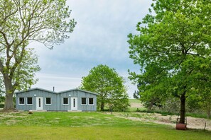 A single-story building with a flat roof, surrounded by a grassy area and trees. - Herthaquelle Appartements - Wohnung 2 "frl. Hertha" - Herthaquelle (Garz/Rügen)