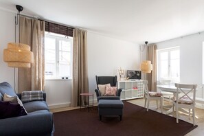 Una sala de estar moderna con un sofá, un reposapiés y una mesita. Hay una silla y un mueble blanco con un televisor.