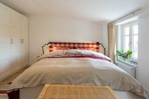 Un dormitorio con cama, ventana con cortinas, radiador y armario.