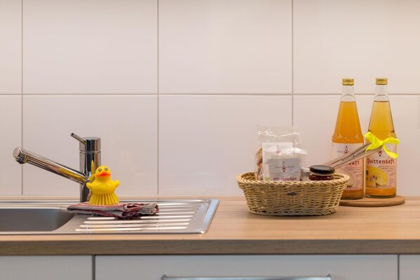 Una encimera de cocina con un lavamanos, un patito de goma, una cesta con objetos y dos botellas de una bebida.
