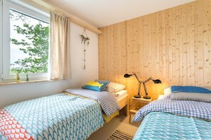 Una habitación con dos camas, una ventana con cortinas, una pared de madera y un escritorio con lámpara.