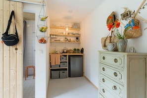 Una cocina compacta con armarios de madera, un refrigerador pequeño y una encimera con diversos utensilios de cocina.