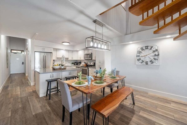 A modern kitchen with white cabinets, a wooden dining table, and a large wall clock.