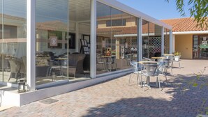 An outdoor cafe with glass walls, wicker furniture, and a tiled roof in the background.