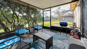 A covered patio with wicker furniture, a table, and a barbecue grill.