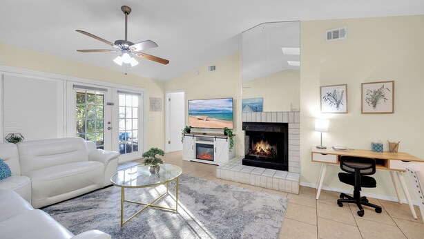 A living room with a white leather sofa, a glass coffee table, a fireplace, a TV, and a desk with a computer.