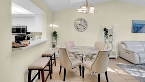 A modern kitchen with a microwave, a white countertop, and a dining area with a glass table and beige chairs.