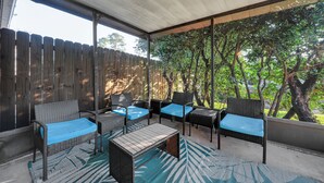 A covered patio with wicker furniture and blue cushions, overlooking a wooden fence and lush greenery.