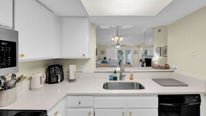 A modern kitchen with white cabinets, a stainless steel sink, a coffee maker, and a dishwasher.