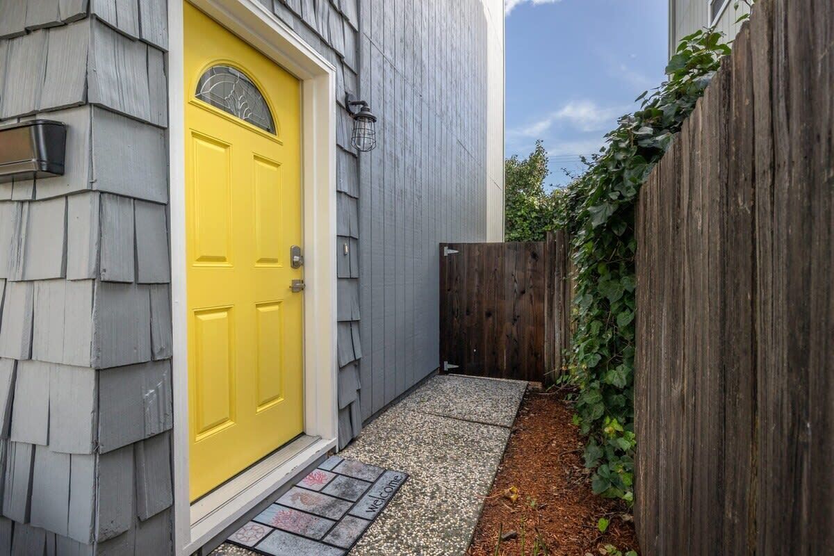 A yellow door with a welcome mat, a wooden fence, and a gravel path.