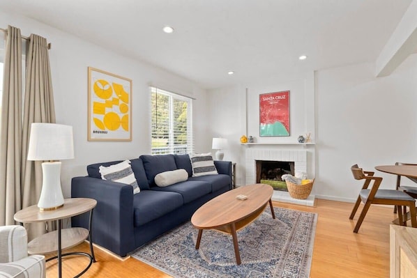 A modern living room with a blue sofa, a round coffee table, and a fireplace. - 3 bedroom home - walk to Twin Lakes & Harbor! (Santa Cruz)
