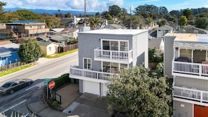 Un immeuble de deux étages doté d’un balcon, situé à l’angle d’une rue, à proximité d’un panneau de signalisation indiquant un arrêt.