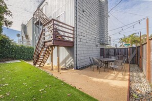 Un bâtiment moderne doté d’une terrasse en bois, d’un escalier et d’un espace patio aménagé avec du mobilier d’extérieur.