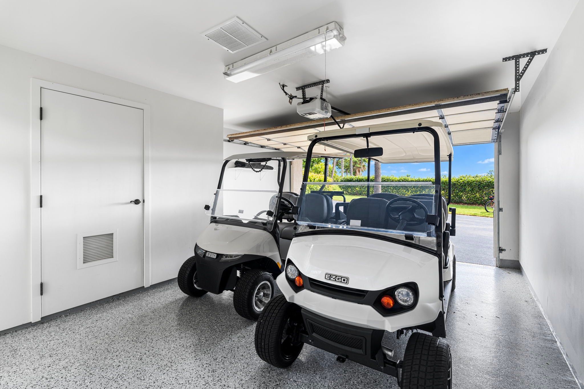 Dos carritos de golf estacionados dentro de un garaje, con vista despejada a un campo de golf.