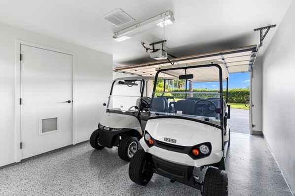Deux voiturettes de golf sont garées à l’intérieur d’un garage, d’où l’on a une vue dégagée sur un terrain de golf.