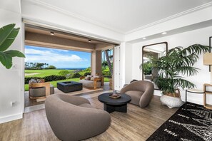 Un salon moderne doté d’une grande porte-fenêtre coulissante donnant sur un espace extérieur privatif, aménagé avec des canapés, une table basse et une plante en pot.
