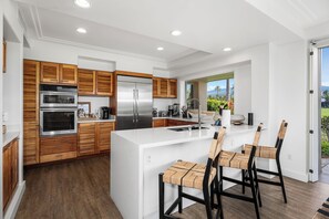 Une cuisine moderne avec des meubles en bois, des appareils en acier inoxydable et un grand îlot central doté de tabourets de bar.