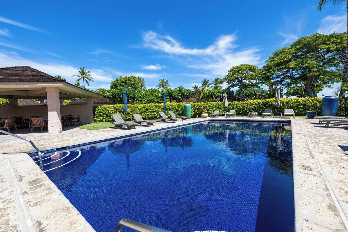 Una piscina con sillas de descanso y una zona de estar techada.