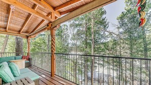 A wooden deck with a cushioned seating area, a metal railing, and a view of a forested area. - Near Hiking Trails: Spacious Cloudcroft Retreat! (Cloudcroft)