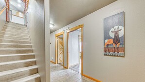 A hallway with a carpeted staircase, a wooden door, and a wall-mounted artwork of deer. - Near Hiking Trails: Spacious Cloudcroft Retreat! (Cloudcroft)