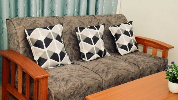 A grey sofa with three patterned cushions, a wooden armrest, and a small table with a potted plant.