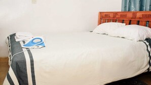 A bed with a striped blanket, a pair of scissors, and an iron on a wooden headboard.