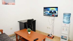 A small room with a wooden table, a black office chair, a TV mounted on the wall, and a water dispenser.