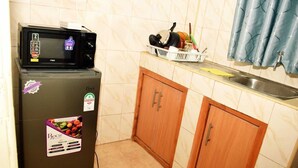 A compact kitchen with a refrigerator, wooden cabinets, a sink, and a blue curtain.