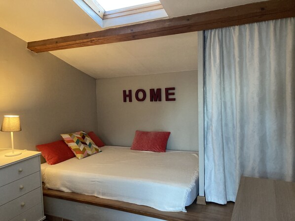 A bedroom with a bed, a nightstand, a lamp, a window with a view, and a 'HOME' sign on the wall.