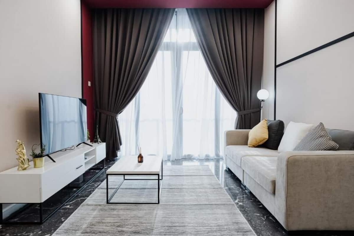 A modern living room with a flat-screen TV, a white sofa with cushions, a coffee table, and a large window with curtains.
