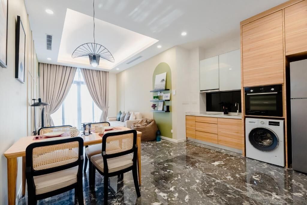 Une cuisine moderne équipée d’un lave-linge intégré, un coin repas avec une table et des chaises, et un luminaire au plafond.
