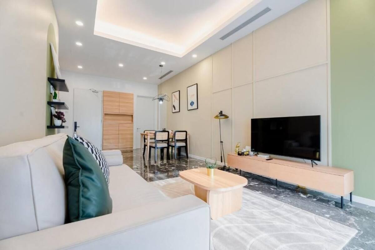 A modern living room with a sofa, coffee table, TV, and dining area.