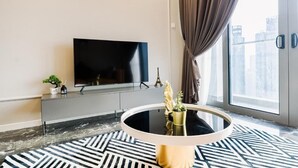 Un salon moderne avec un grand téléviseur à écran plat fixé au mur, une table basse ronde dotée d’un pied doré et un tapis à motifs sur le sol.