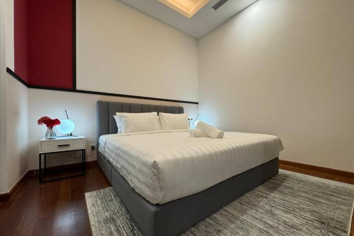 A modern bedroom with a large bed, a bedside table with a lamp, and a red accent wall.
