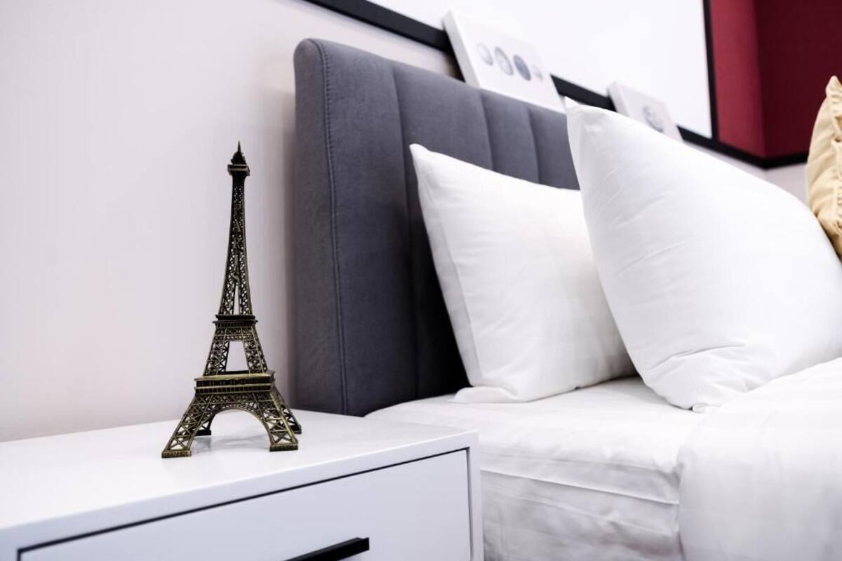 A bed with white bedding, a grey headboard, and a small Eiffel Tower model on a bedside table.