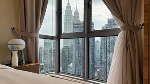 Une chambre d’hôtel dotée d’une grande fenêtre donnant sur le paysage urbain, avec notamment des immeubles de grande hauteur.