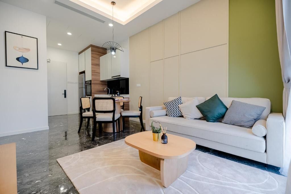 A modern living room with a white sofa, a wooden coffee table, and a dining area with chairs and a table.