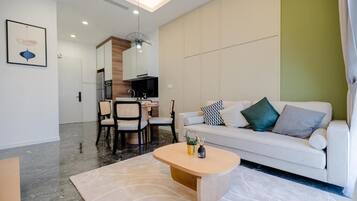 A modern living room with a white sofa, a wooden coffee table, and a dining area with chairs and a table.