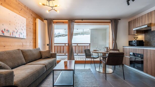 A modern interior with a sofa, dining table, chairs, a kitchen area, and a large window with a view.