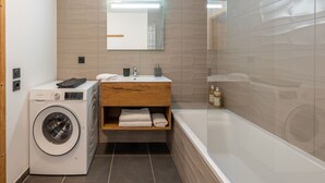 A modern bathroom with a washing machine, a wooden vanity, a mirror, and a bathtub.